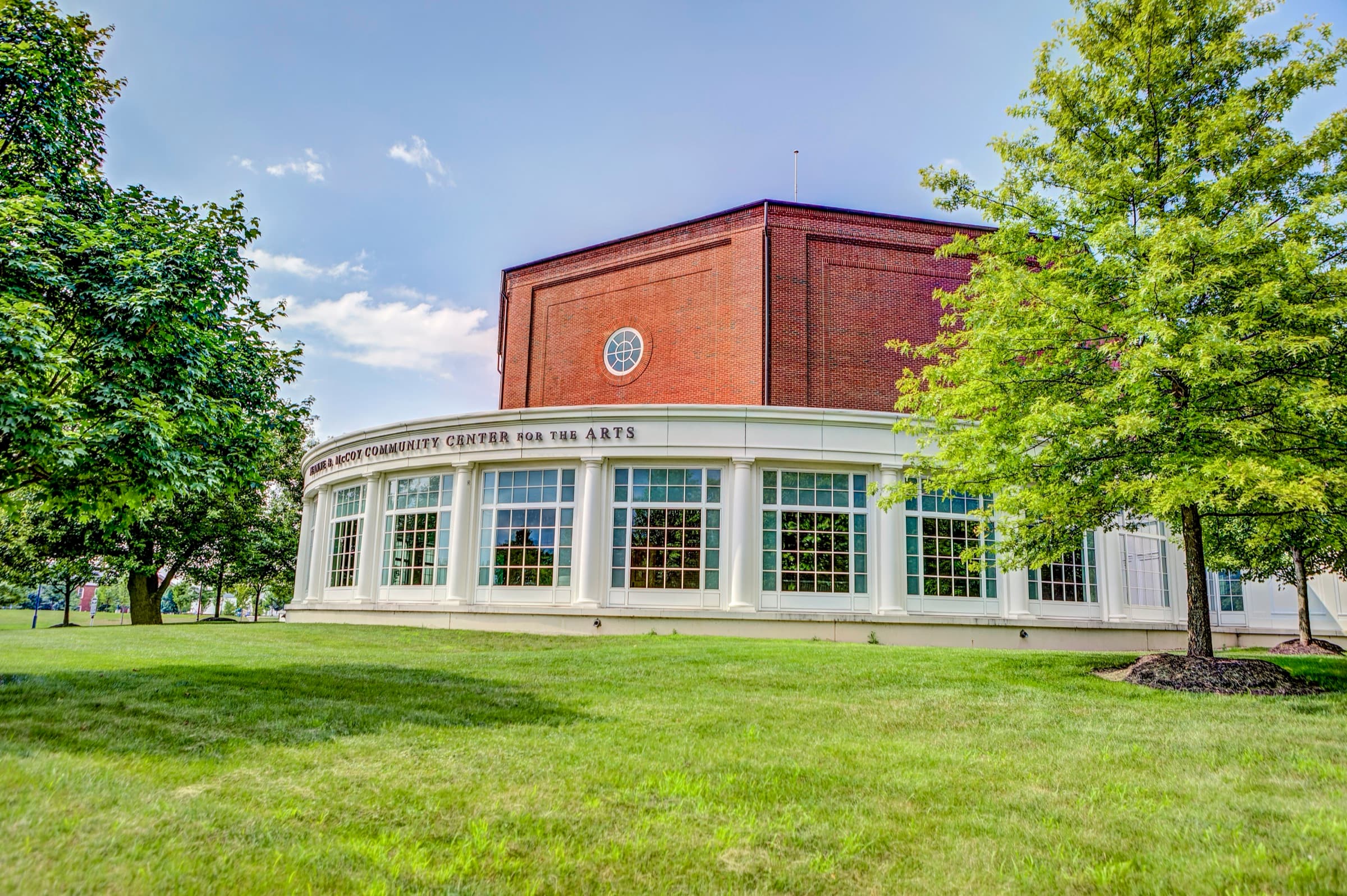 The white-columned, curved glass facade of the Jeanne B. McCoy Community Center for the Arts framed by green lawn